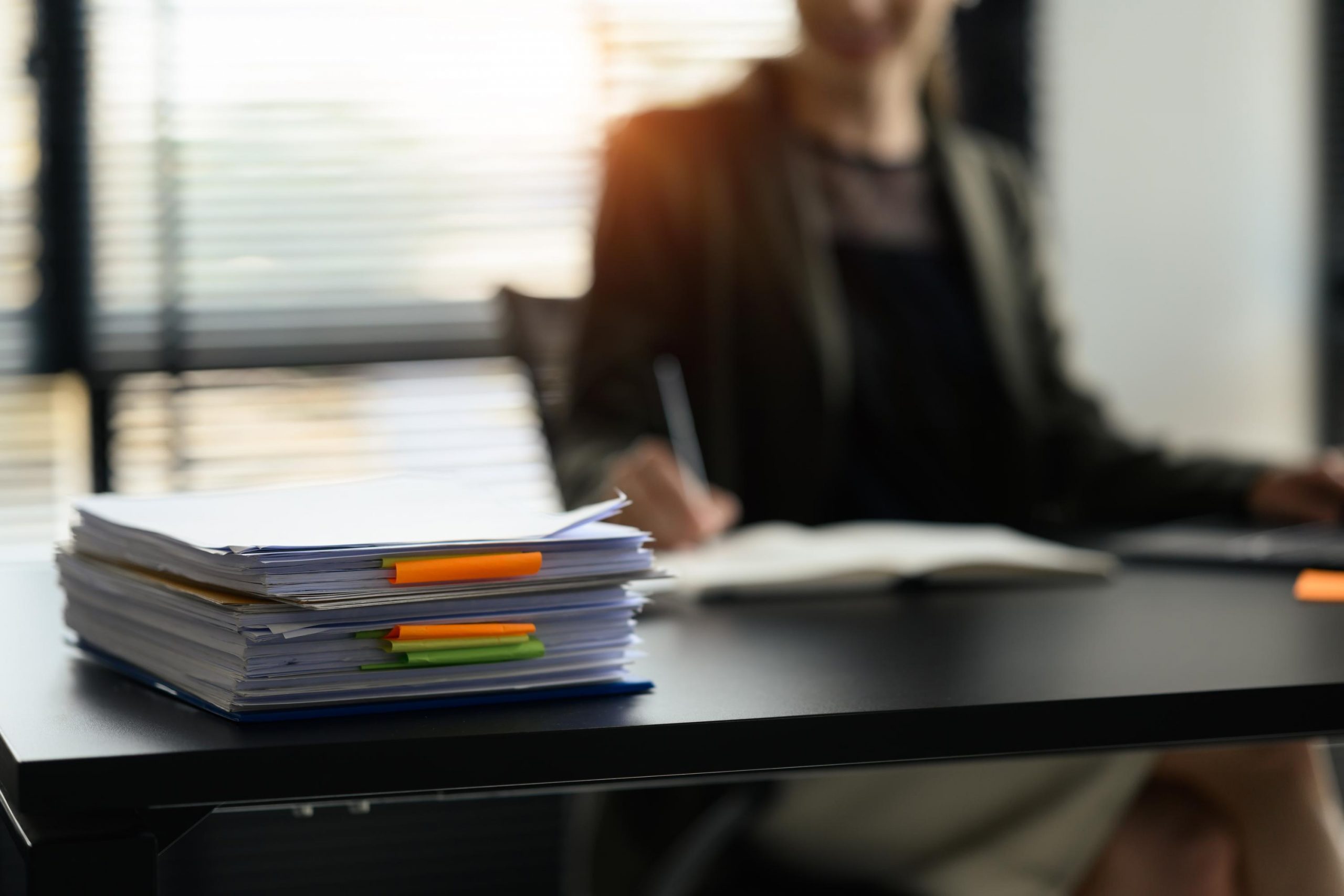 Stack of paper files with colorful sticky notes on office desk. Organized document management system concept.