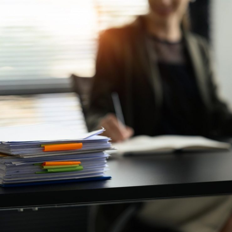 Stack of paper files with colorful sticky notes on office desk. Organized document management system concept.