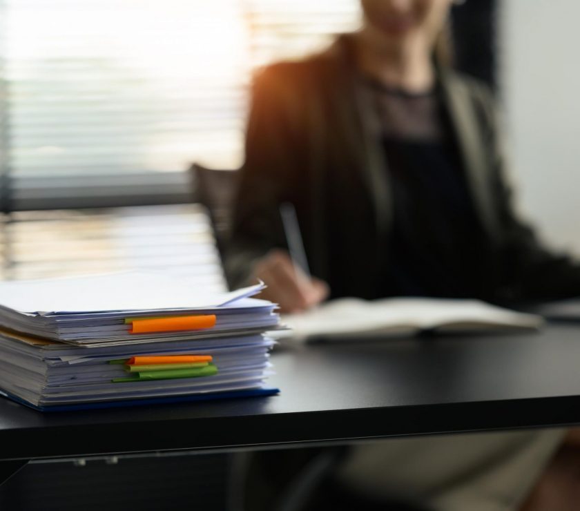 Stack of paper files with colorful sticky notes on office desk. Organized document management system concept.