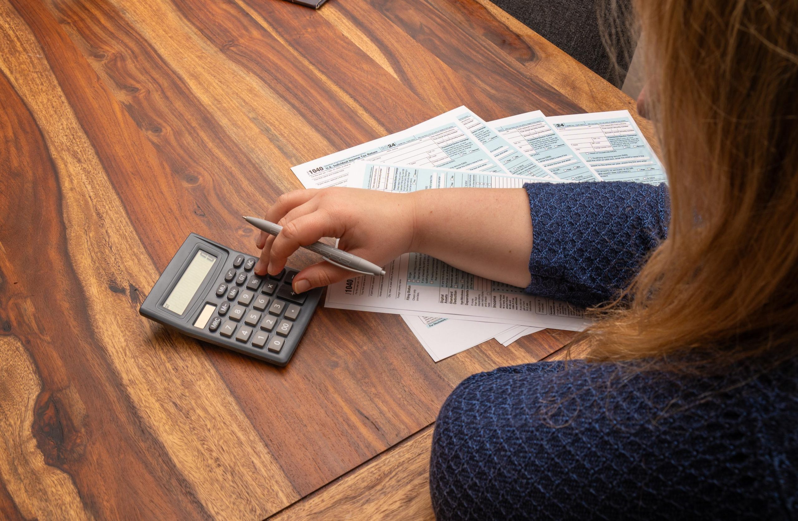 Woman managing finances by filling out 1040 US income tax form at a wooden desk