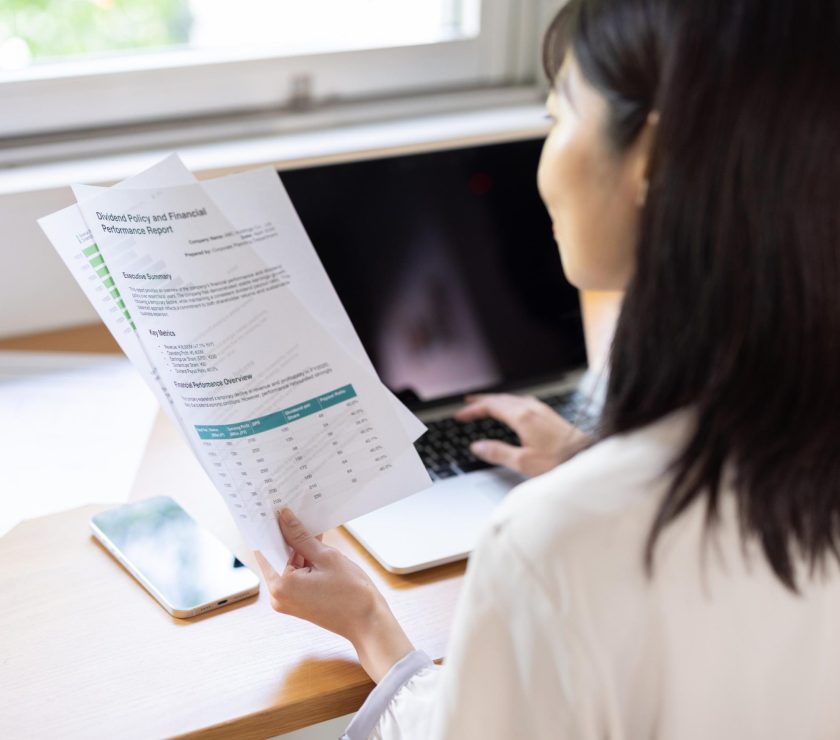 Back view of woman working on laptop while holding document at window