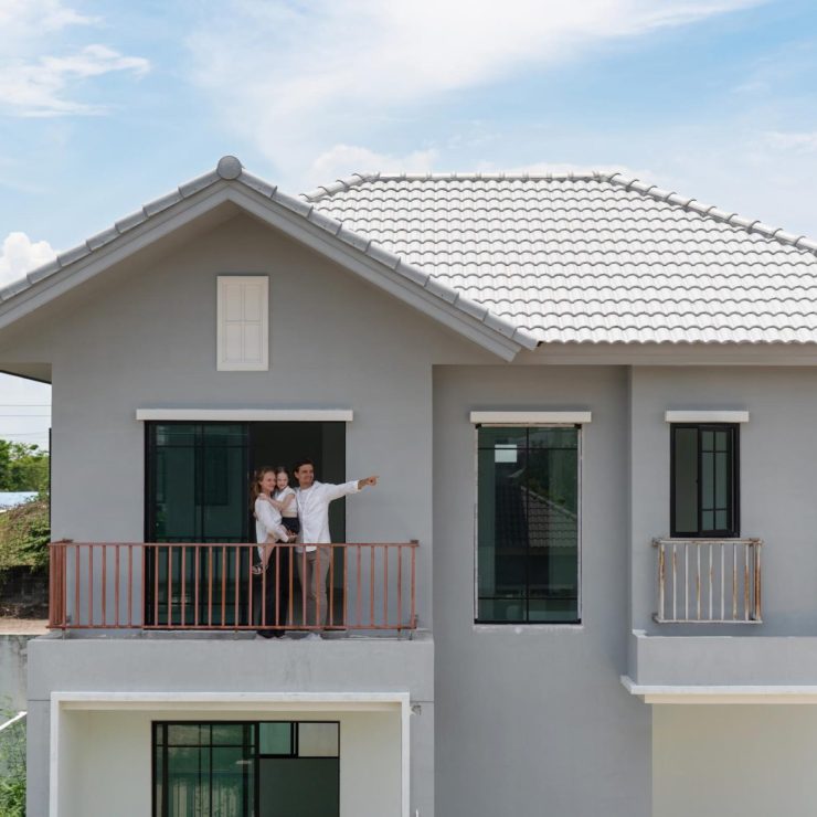 A cheerful family stand on the balcony of a newly constructed modern house, pointing at the landscape. Clear sky and a vibrant setting create a cheerful ambiance in this lively area.