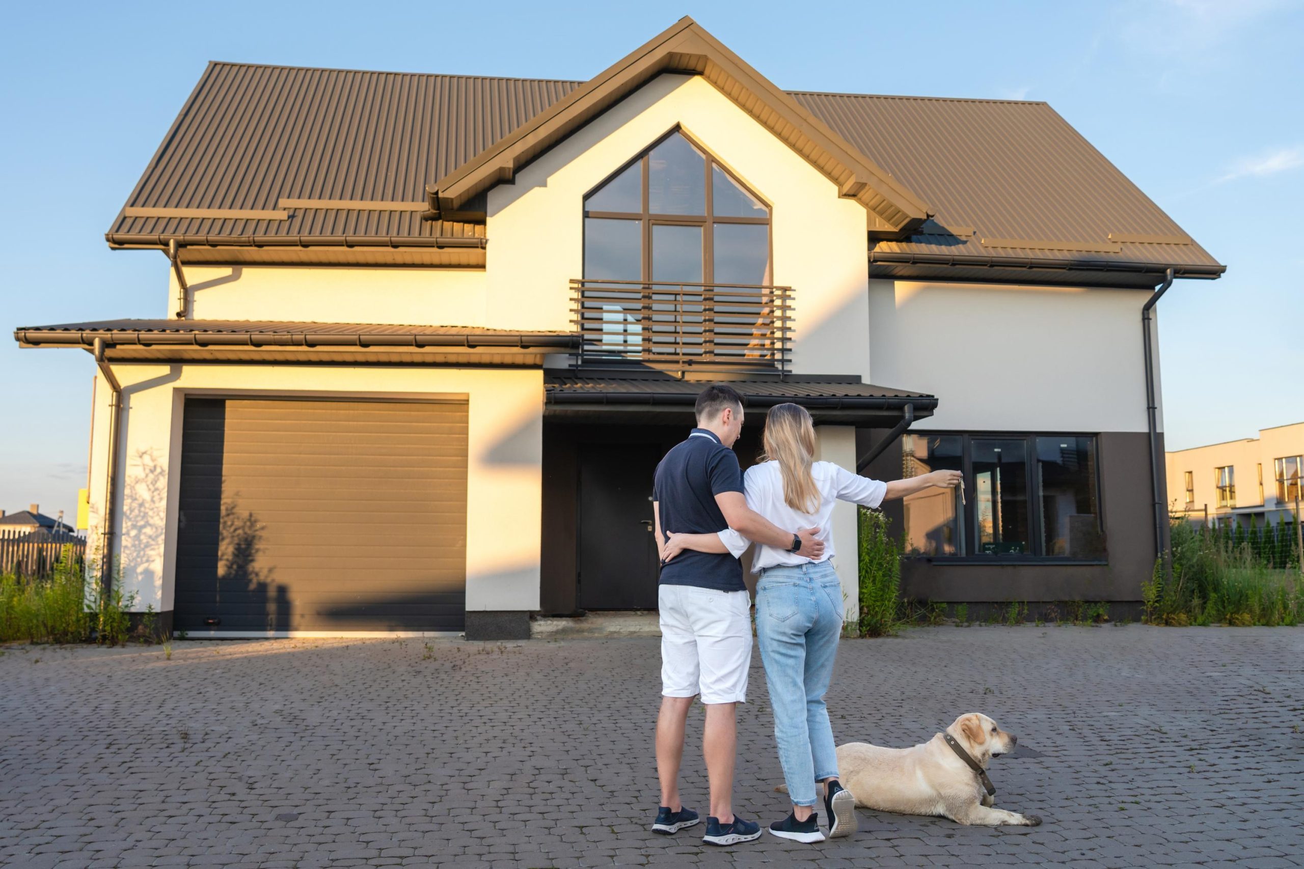 Happy young couple with dog holding their keys in front of residential home. Property lease real estate for relocation. Leasing insurance and purchase. Buying or renting