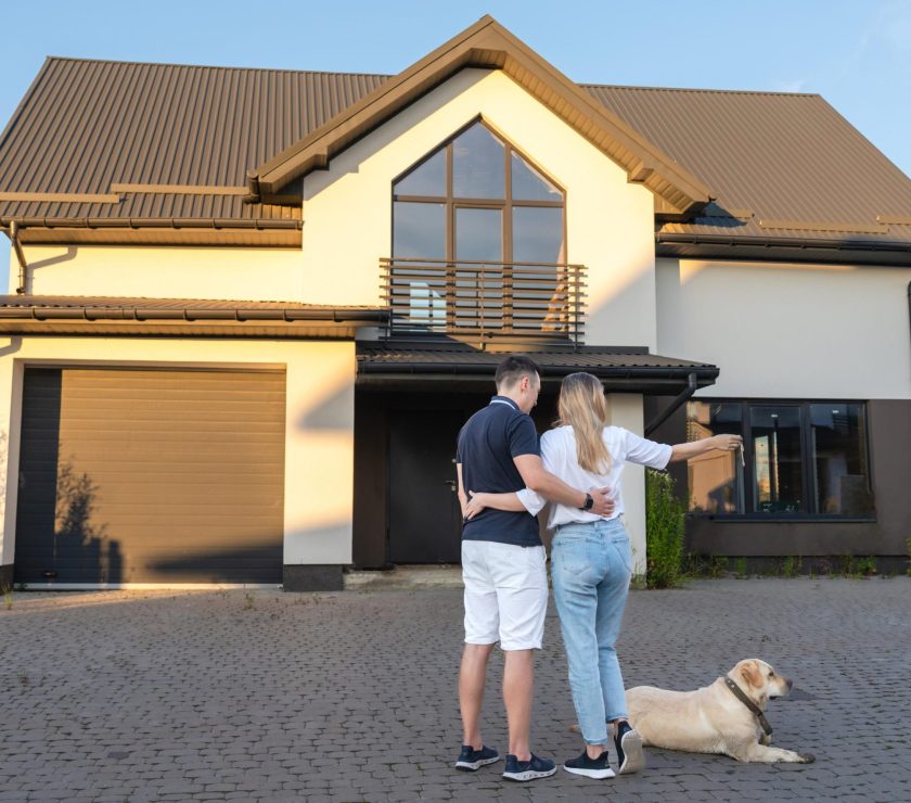 Happy young couple with dog holding their keys in front of residential home. Property lease real estate for relocation. Leasing insurance and purchase. Buying or renting