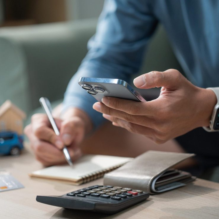 Man hand using smart phone and calculator to manage monthly expenses, saving for house and car, personal finance budget planning concept at home